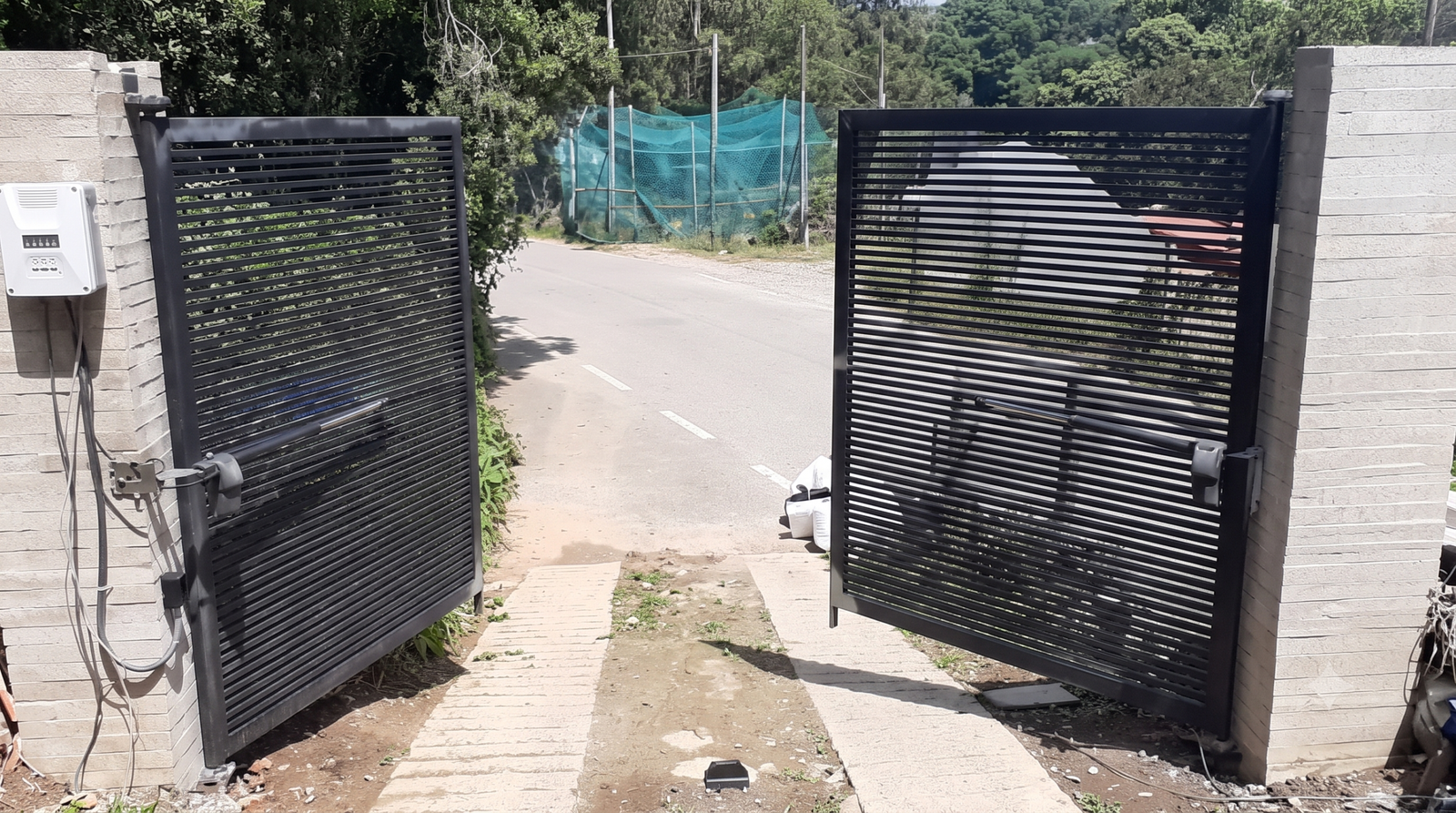 Portón automatizado de dos hojas con brazos motorizados y control de acceso instalado en el acceso a una vivienda.